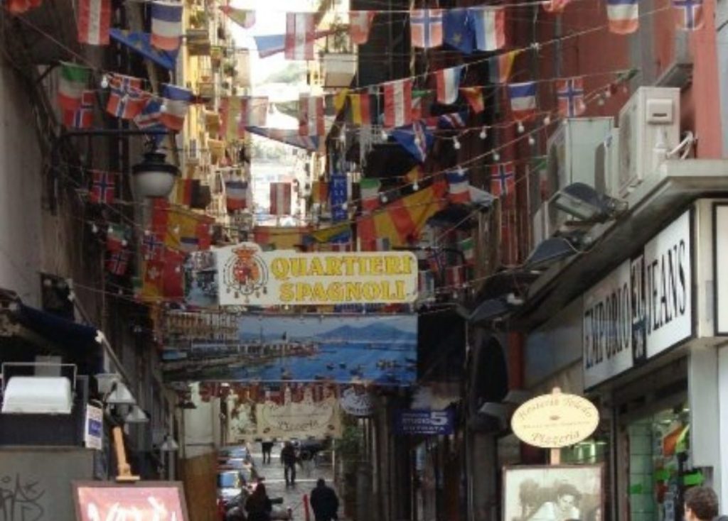 A narrow street in the Quartieri Spagnoli, Naples, strung with flags and a sign reading Quartieri Spagnoli