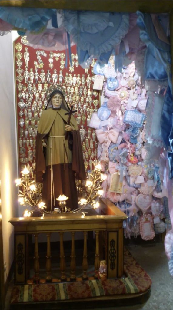 A saint's statue in Naples surrounded by hundreds of silver ex-votos and pink and blue ribbons