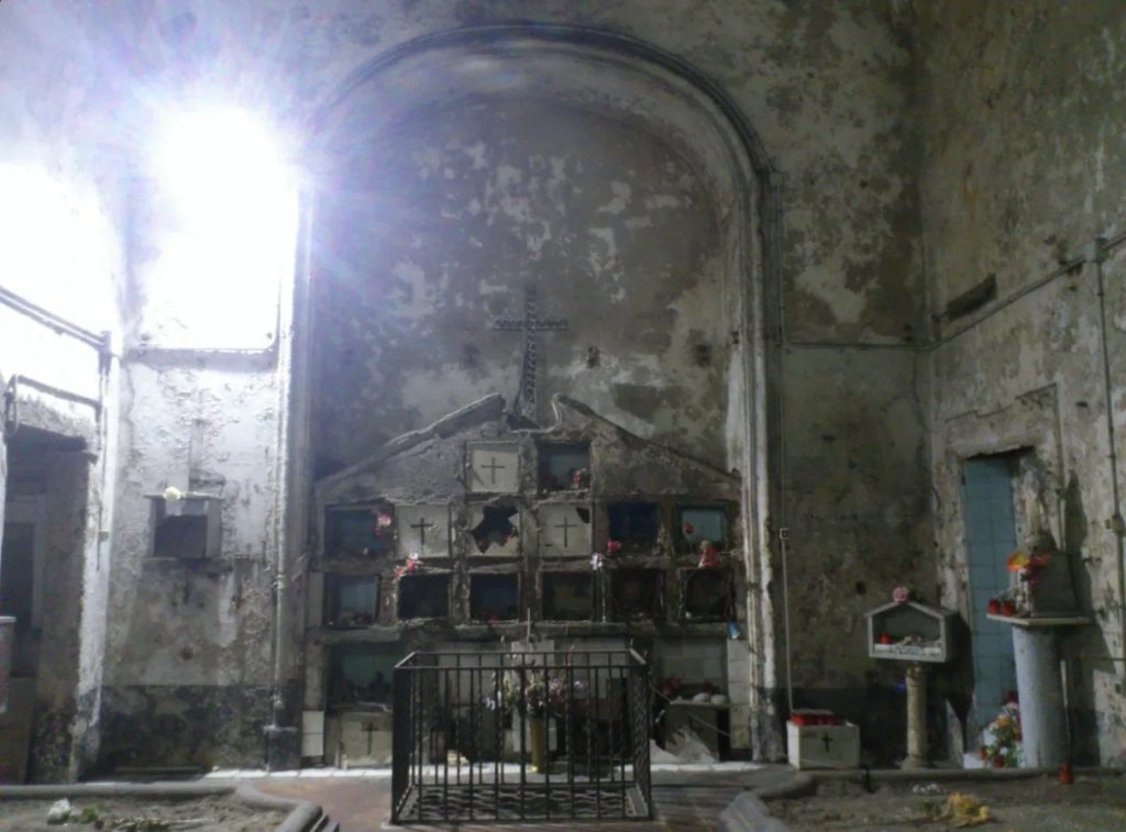 Shrine to the anime pezzentelle in Naples, with old niches, crosses, flowers and offerings inside a weathered chapel-like space.