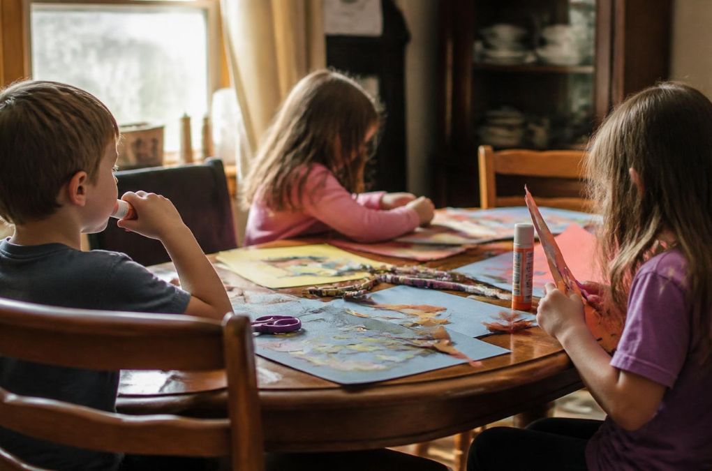 Children doing arts and crafts at a table, one holding a glue stick, evoking a real classroom moment behind Loveandpizza.it