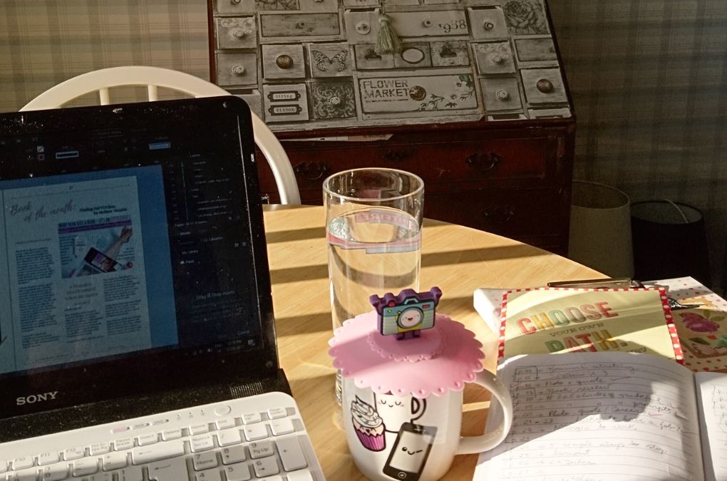 A laptop showing a magazine-style book review layout beside a mug and an open notebook