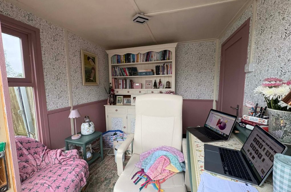 A cosy garden writing shed with a bookshelf, armchair, sofa and two laptops open on a desk