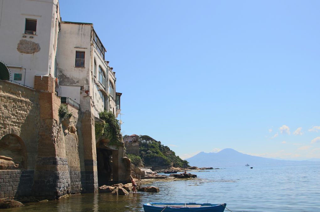 The seaside village of Marechiaro in Posillipo, with fishing boats, old buildings above the water and Mount Vesuvius across the bay
