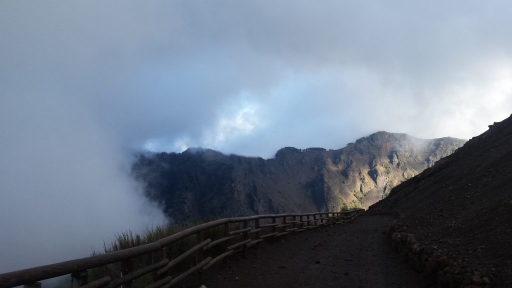 The rim of the Vesuvius crater with cloud pouring over the edge, seen from the wooden fence beside the walking path